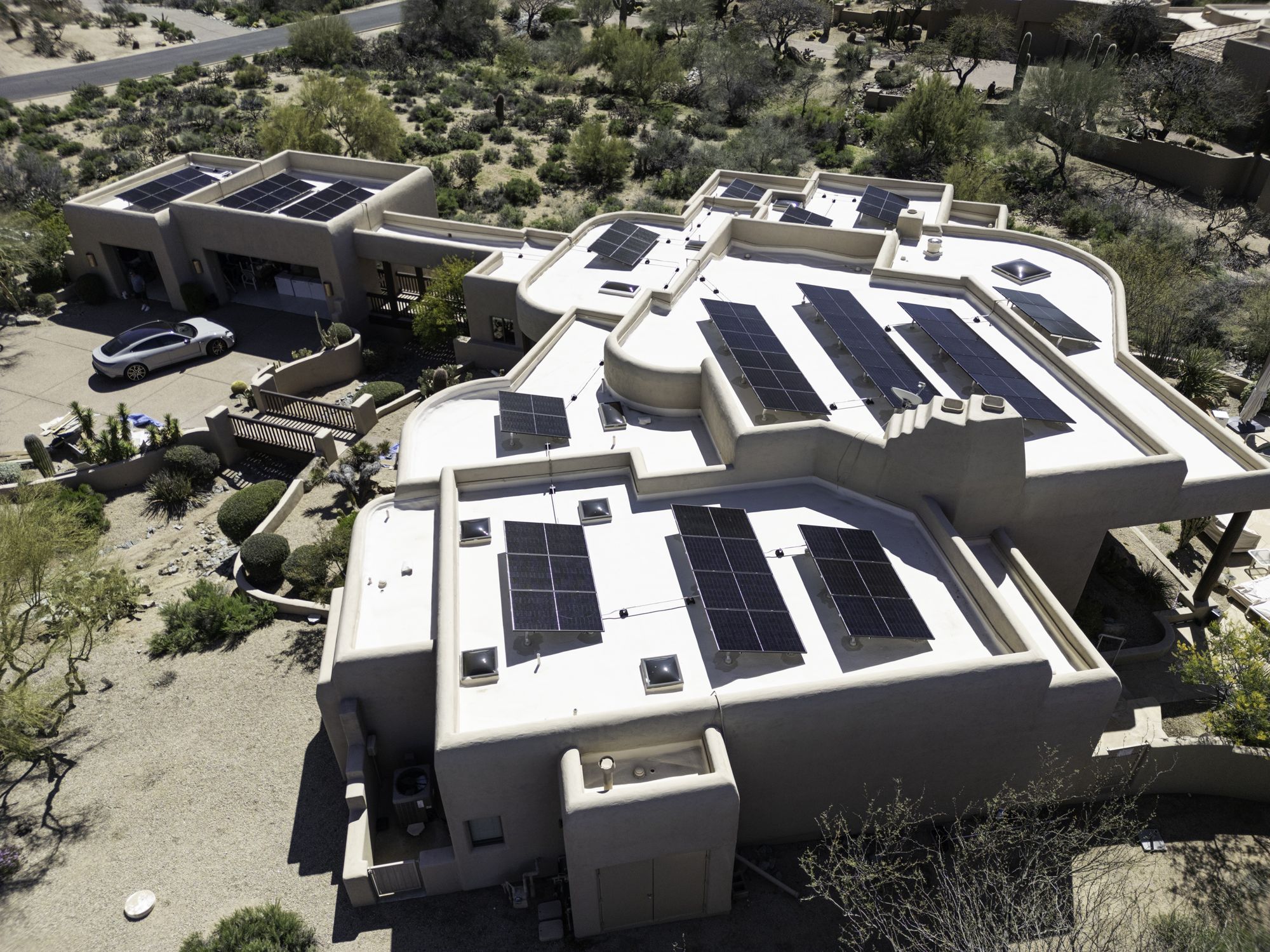 Aerial view of a desert home with solar arrays across its flat roofs