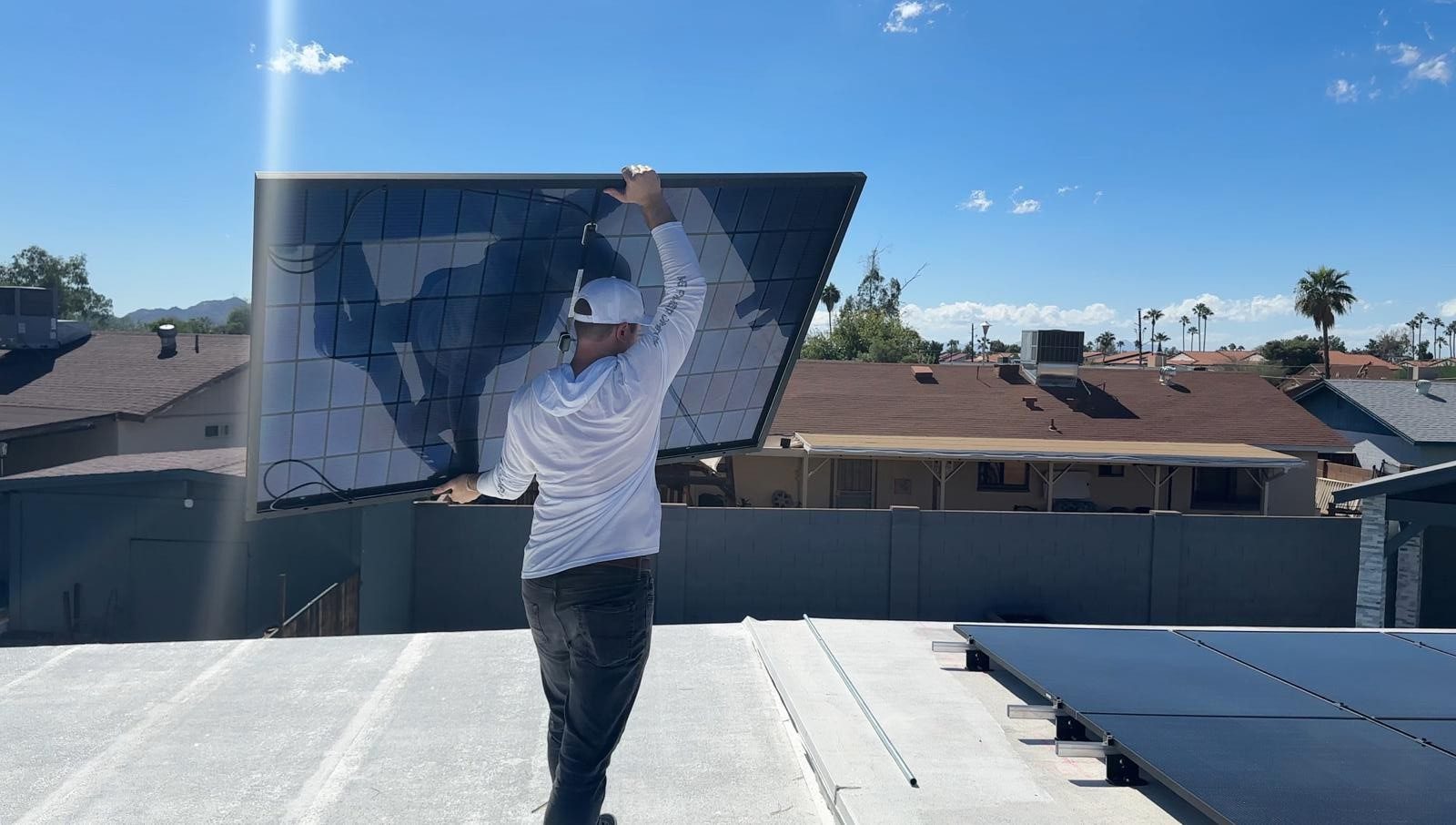 A man carrying a solar panel across a flat roof