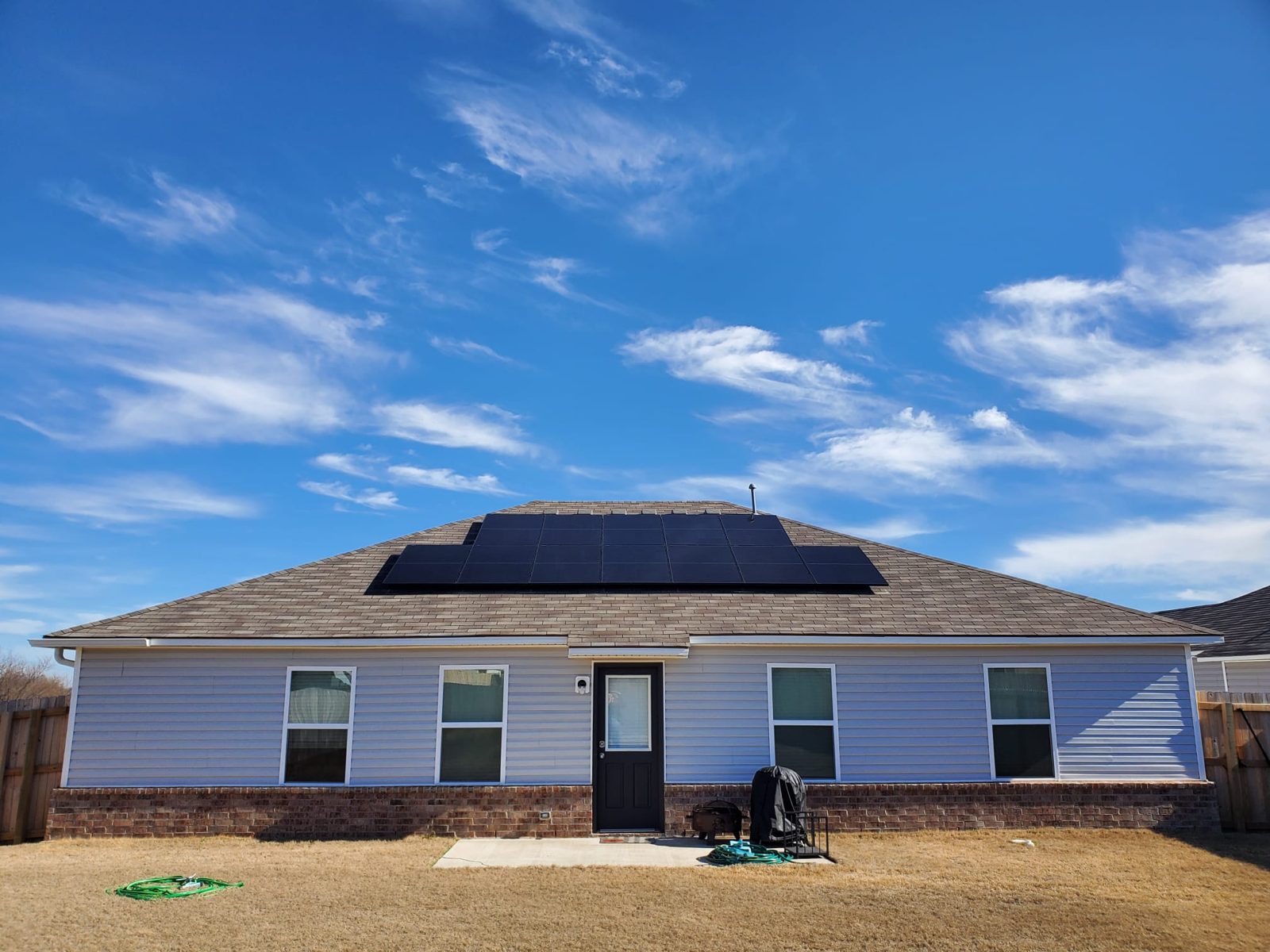 Solar panels centered on the roof of a single-story home under a blue sky